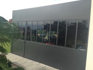 Verrière extérieure noire style atelier avec porte battante sur une terrasse pavée.