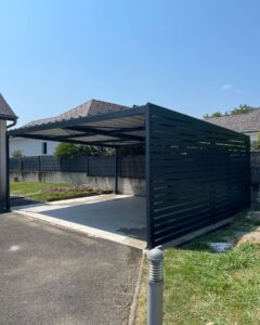 Carport moderne en métal noir avec paroi à claire-voie sur dalle béton.