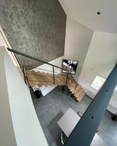 Escalier en bois suspendu avec rampe noire sur sol en carrelage gris et mur d'accent texturé.
