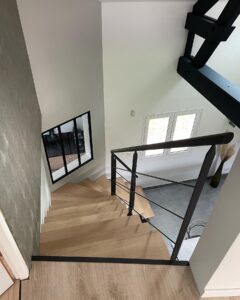 Escalier tournant en bois clair et rampe noire vue de haut dans un intérieur moderne et lumineux.