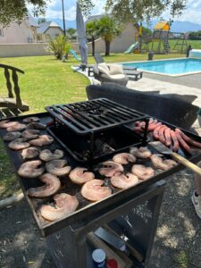Grillade de pancetta et saucisses sur plancha extérieure près d'une piscine.